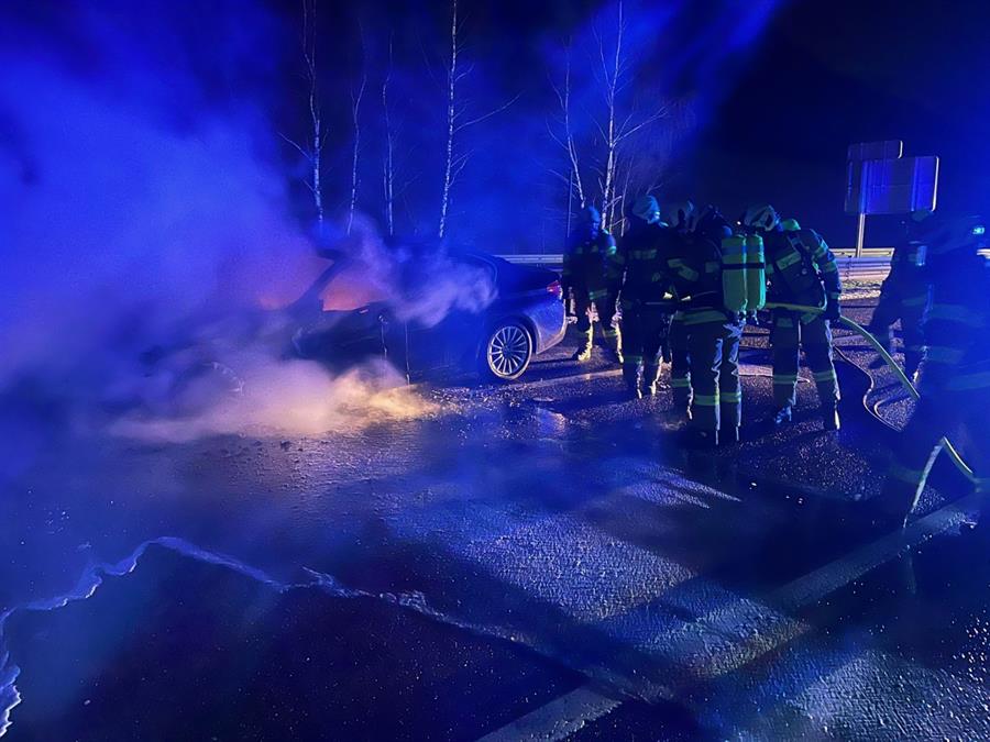 Eine Gruppe von Menschen, die neben einem brennenden Auto stehen